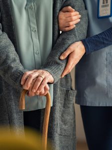 Nurse helping elderly patient with wooden walking stick