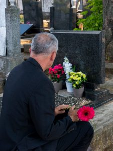 Man sitting at graveside with flowers