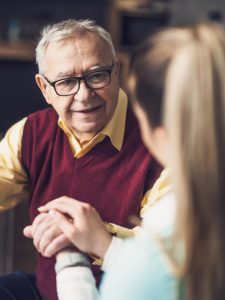 Woman talking to elderly man and holding his hand