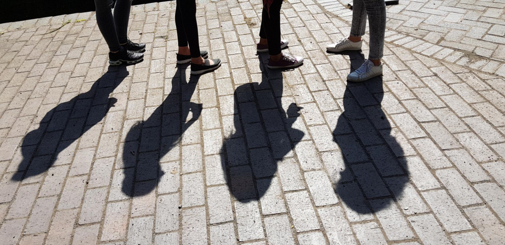 Young people's legs and feet standing on cobbles with strong sunlight and shadows